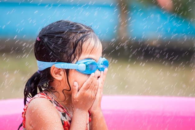 Occhiali di protezione d&#39;uso di nuoto della ragazza asiatica felice del piccolo bambino divertendosi per giocare acqua nella cacca