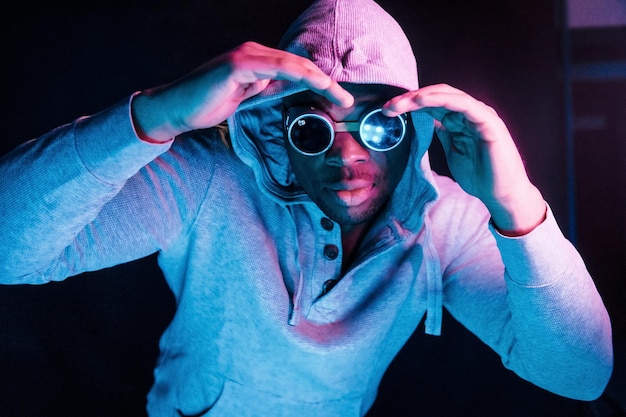 Occhiali in stile cyberpunk Illuminazione al neon futuristica Giovane uomo afroamericano in studio