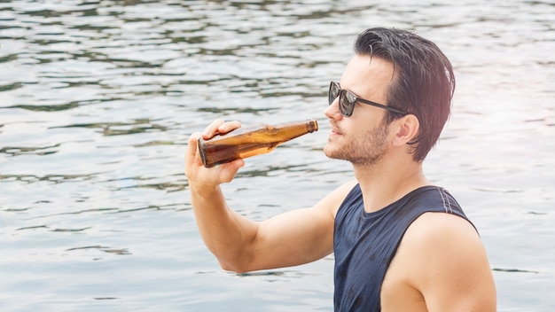 occhiali neri uomo con una bevanda di bottiglia di birra in piscina