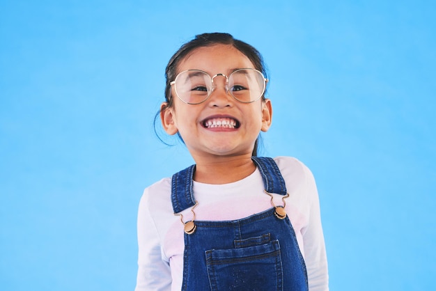 Occhiali per bambini e vista in studio con sorriso medico e pensiero per la cura degli occhi su sfondo blu Occhiali da prova per bambine e modella giovane con montatura per lenti ed entusiasta per la salute