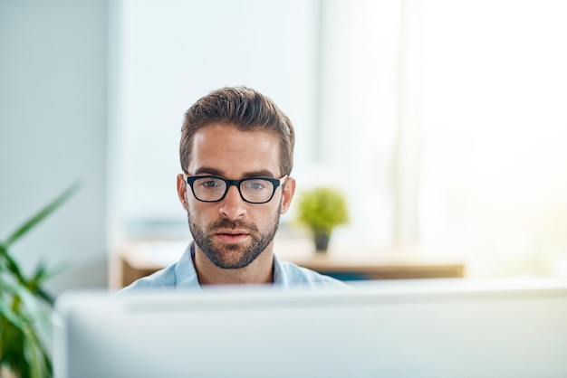 Occupato al lavoro come al solito Inquadratura di un giovane uomo d'affari che lavora su un computer in un ufficio