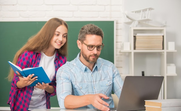 Occupato padre e figlio studiano a scuola con libro e laptop su sfondo lavagna genitorialità