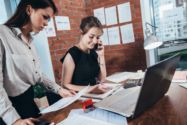 Occupato top manager femminile parlando al telefono mentre il suo assistente mostra le sue statistiche finanziarie.