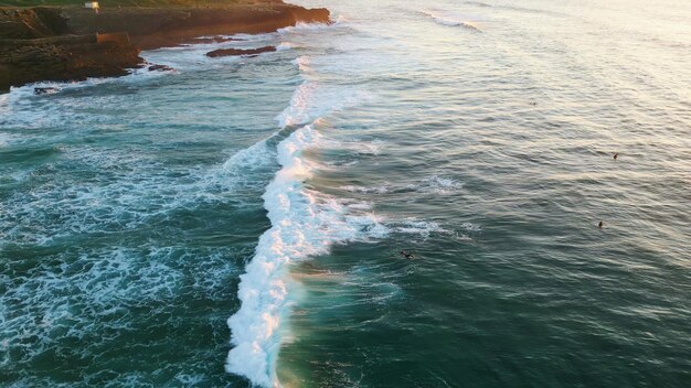 Oceano blu profondo schiumante rotolante sulla riva rocciosa vista aerea surfisti in attesa di onde