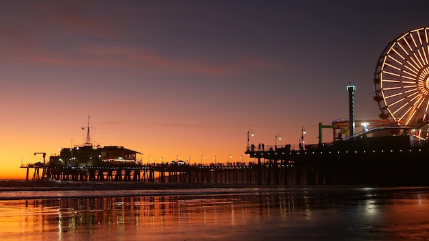 Oceano crepuscolare e ruota panoramica illuminata, parco di divertimenti sul molo. Spiaggia di Santa Monica, USA.