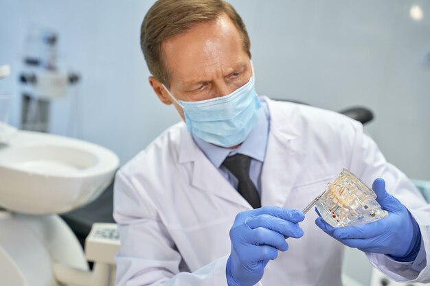 Odontotecnico concentrato in maschera che tiene un modello di denti