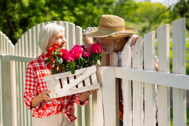 Odore di fiori rosa. Uomo barbuto che indossa un cappello di paglia che odora di fiori rosa mentre parla con il vicino