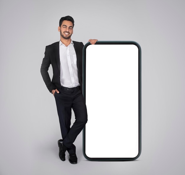 Offerta mobile Sorridente uomo d'affari arabo appoggiato al grande smartphone vuoto