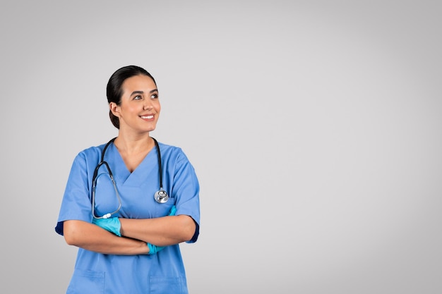 Offerta sanitaria dottoressa latina positiva in uniforme blu in posa con lo stetoscopio che guarda da parte