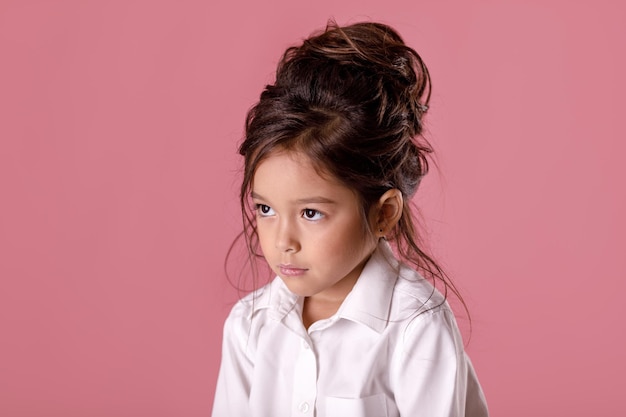 Offeso triste bambina annoiata in camicia bianca su sfondo rosa. Emozioni umane ed espressione facciale