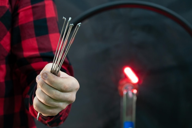 Officina ciclistica professionale Il meccanico tiene i raggi in mano su sfondo nero Un meccanico di biciclette moderno e alla moda con una camicia a quadri rossa sullo sfondo di una ruota