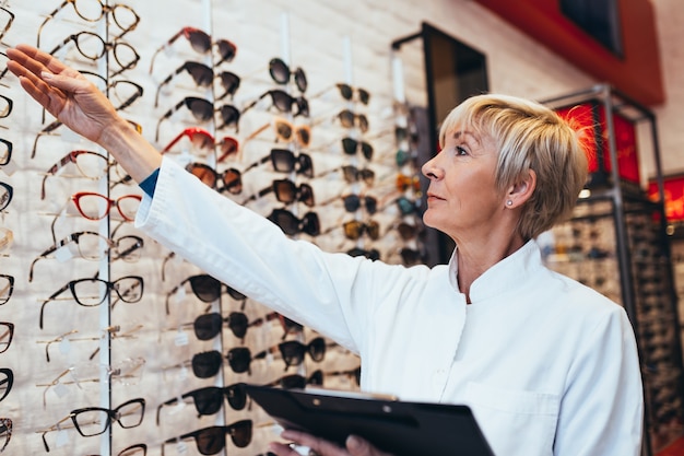 Oftalmologo femminile senior che sceglie il telaio degli occhiali per il suo cliente nel negozio di ottica.