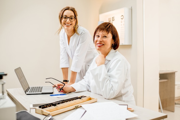 Oftalmologo senior della donna con la giovane assistente femminile che lavora con il computer portatile all'ufficio