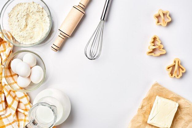 Oggetti e ingredienti per la cottura di stampi in plastica per biscotti su sfondo bianco Farina uova mattarello frusta latte crema di burro Vista dall'alto spazio per il testo