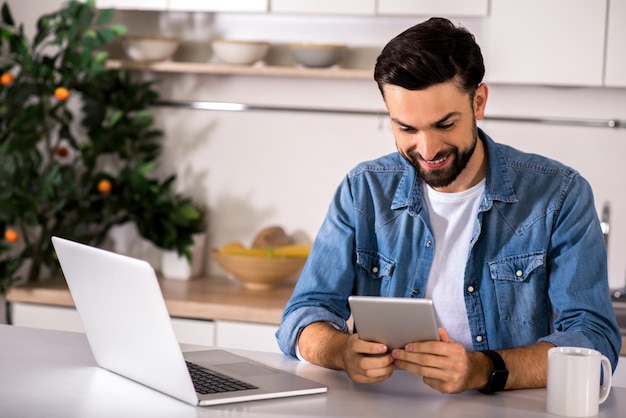 Ogni giorno utente Allegro bell'uomo seduto in cucina e usando il suo tablet