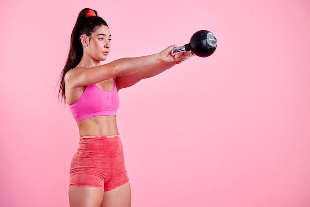 Ogni sfida ha lo scopo di cambiarti Foto in studio di una giovane donna sportiva che si esercita con un kettlebell su uno sfondo rosa