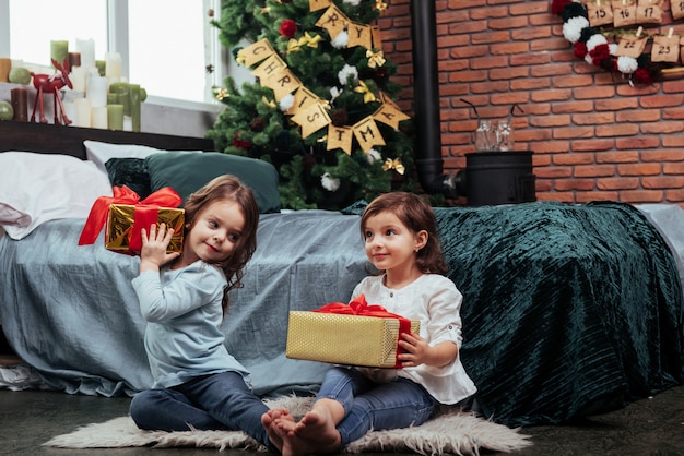 Ognuno di loro ha un bel regalo. Vacanze di Natale con regali per questi due bambini seduti nella bella stanza vicino al letto