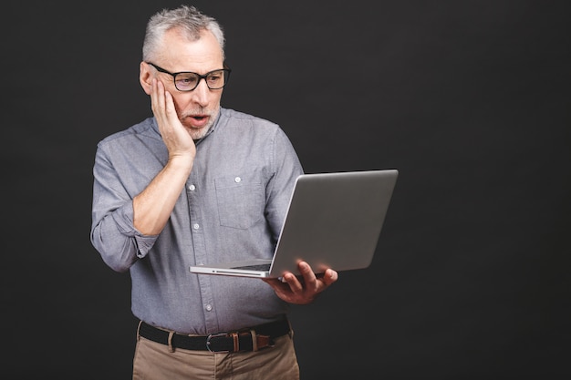 OH MIO DIO! Sono scioccato! Uomo anziano barbuto invecchiato senior spaventato in occhiali che tengono computer portatile