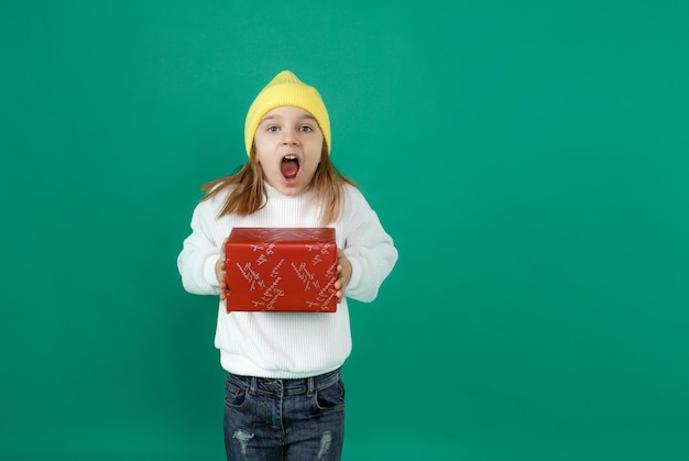 Oh. Un bambino eccitato tiene in mano una confezione regalo e urla di gioia, bocca aperta, muro verde. le emozioni dei bambini