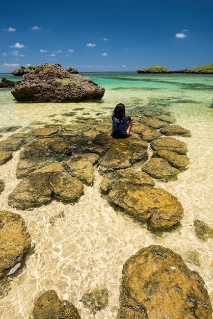 Okinawa ragazza seduta sulle rocce presso la spiaggia di Hoshizuna con le sue acque cristalline contemplando il paesaggio, isola di Iriomote.