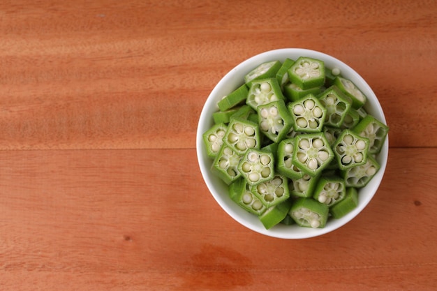 Okra o Ladys finger o Bhindi verdura verde fresca disposta su una ciotola bianca piena di anelli di okra affettati con sfondo di legno messa a fuoco selettiva vista dall'alto