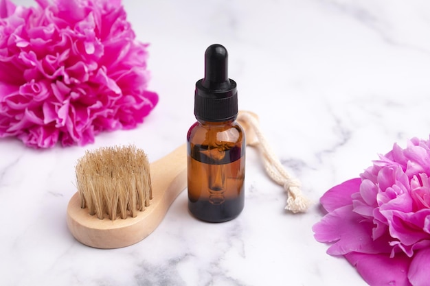 Olio cosmetico in flacone contagocce di vetro e spazzola massaggiante su fondo di marmo con peonie Cosmetici per la cura della pelle Concetto di bellezza per la cura del corpo del viso