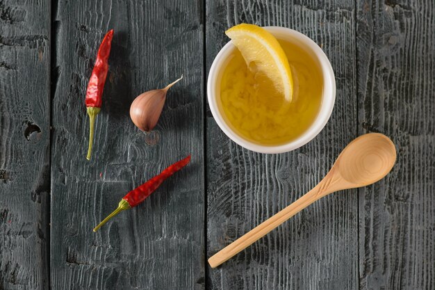 Olio d'oliva con aglio, pepe e limone in una ciotola bianca su un tavolo di legno. Condimento per insalata dietetica. La vista dall'alto.