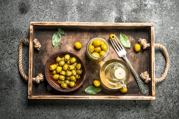 Olio d'oliva con olive in salamoia onn vecchio vassoio sul tavolo rustico.