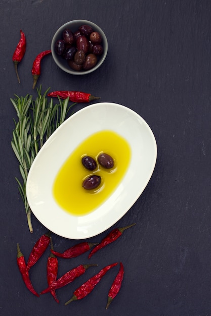 Olio d'oliva con olive, peperoncino e rosmarino sulla superficie nera