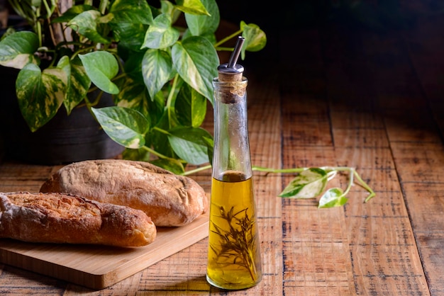Olio d'oliva con rosmarino in una bottiglia di vetro sulla tavola di legno con i panini