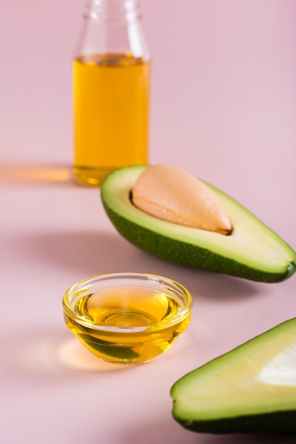 Olio di avocado in una ciotola e metà di avocado su sfondo rosa Cura della bellezza domestica Vista verticale