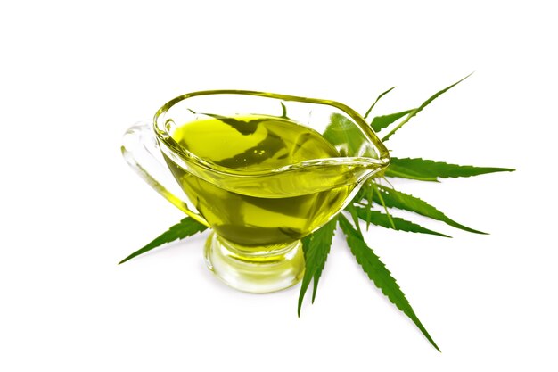 Olio di canapa in una salsiera di vetro, foglie di cannabis e gambi isolati