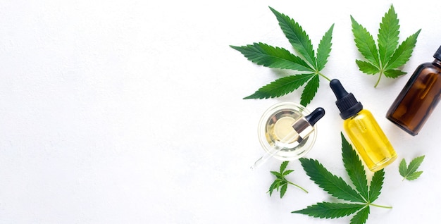 Olio di cannabis in bottiglia di olio di canapa e foglie di cannabis su sfondo bianco. Vista dall'alto, copia dello spazio. Banner