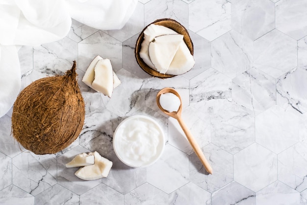 Olio di cocco fresco in un barattolo e cucchiaio e pezzi di cocco sul tavolo Cosmetici naturali Vista dall'alto