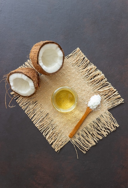 Olio di cocco in un barattolo e noci di cocco fresche su un tavolo scuro. Cosmetici naturali.