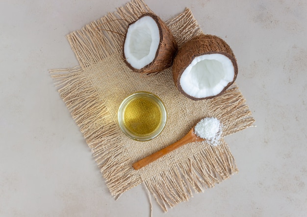 Olio di cocco in un barattolo e noci di cocco fresche su una superficie beige. Cosmetici naturali.