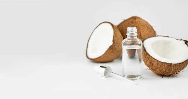 Olio di cocco in una bottiglia con noci di cocco su una tavola bianca. Concetto di cura della pelle. Cosmetici per il viso. Copia spazio.