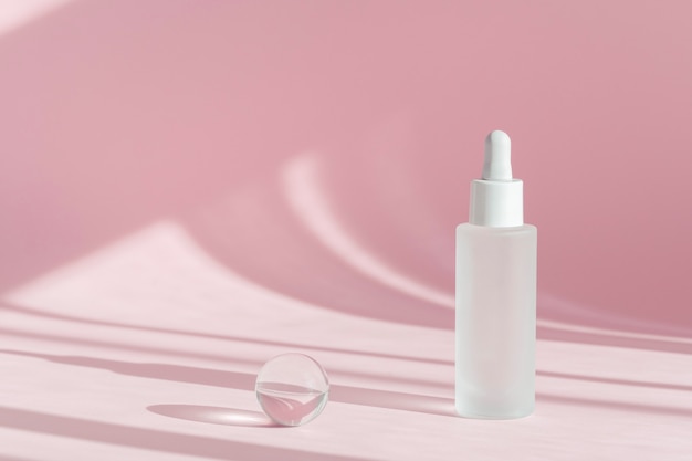 Olio di siero con collagene e peptide in flacone trasparente bianco con contagocce su sfondo rosa decor