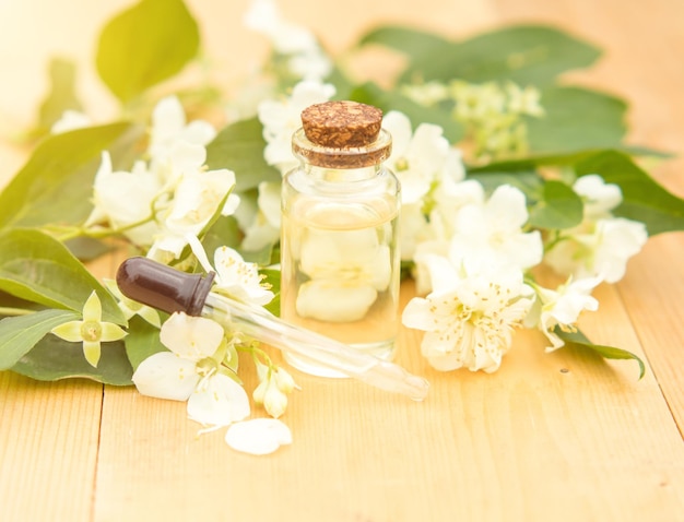 Olio essenziale di gelsomino in una bottiglia di vetro su uno sfondo di fiori di gelsomino su un tavolo di legno