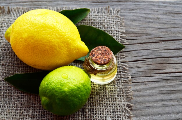 Olio essenziale di limone in una bottiglia di vetro con frutti freschi di limone e lime. Olio di limone per spa, aromaterapia e cura del corpo. Estrarre l'olio di limone. Messa a fuoco selettiva.