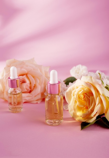 Olio essenziale di rosa in flacone cosmetico vicino a fiori di rosa freschi su sfondo rosa.