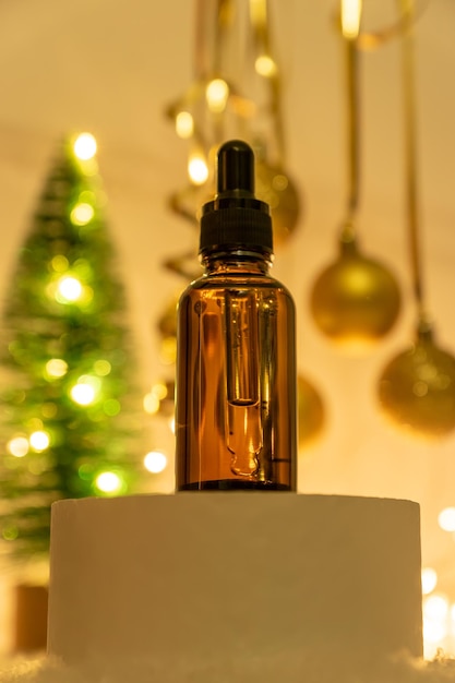 Olio essenziale per il viso con ingredienti naturali sul podio sullo sfondo festivo del nuovo anno con tre di natale e palline. Regali di Capodanno o Natale di prodotti per la cura della pelle e cosmetici.