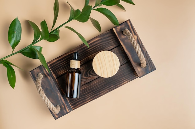 Olio essenziale per il viso o vasetto di siero e crema con confezione con coperchio in bambù su vassoio di legno su sfondo beige Prodotto cosmetico di bellezza per il concetto di cura della pelle