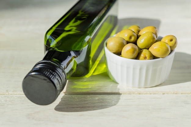 olio extra vergine di oliva in bottiglia verde e olive verdi fresche sul tavolo di legno.