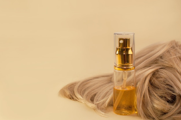 Olio per capelli in un tubo con un erogatore accanto ai capelli della bionda su fondo beige