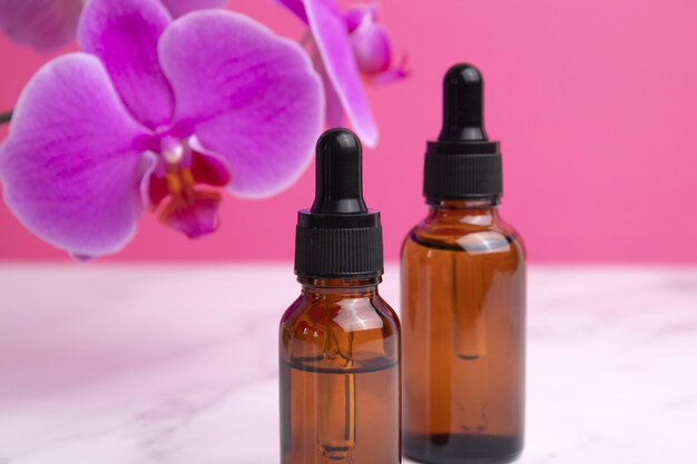 Olio per il viso al collagene di bellezza in flaconi contagocce di vetro con fiori di orchidea Scatto alla moda di imballaggi cosmetici Olio essenziale con ingredienti naturali