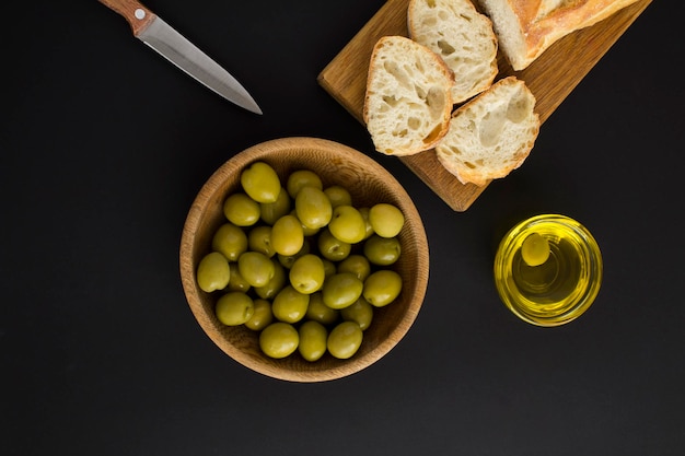 Oliva verde nella ciotola e baguette su sfondo nero Vista dall'alto Spazio copia