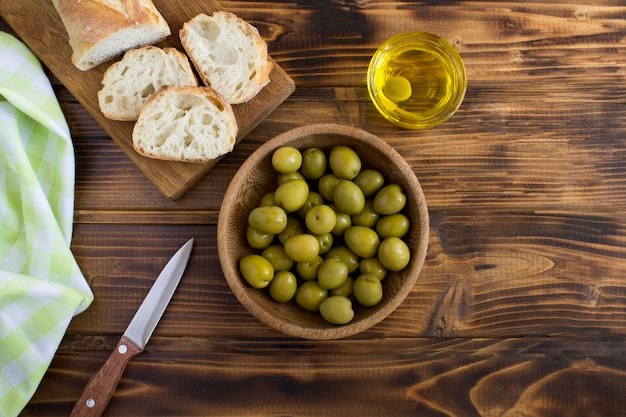 Oliva verde nella ciotola e baguette sullo sfondo di legno Vista dall'alto Copia spazio