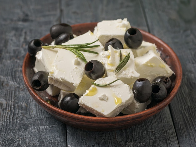 Olive ed erbe aromatiche con fette di formaggio feta su un tavolo di legno. Formaggio naturale prodotto con latte di pecora.