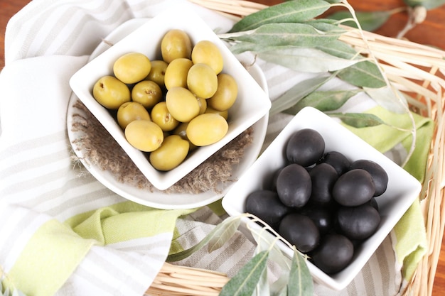 Olive in ciotole con ramo su tovagliolo in cestino sulla tavola di legno